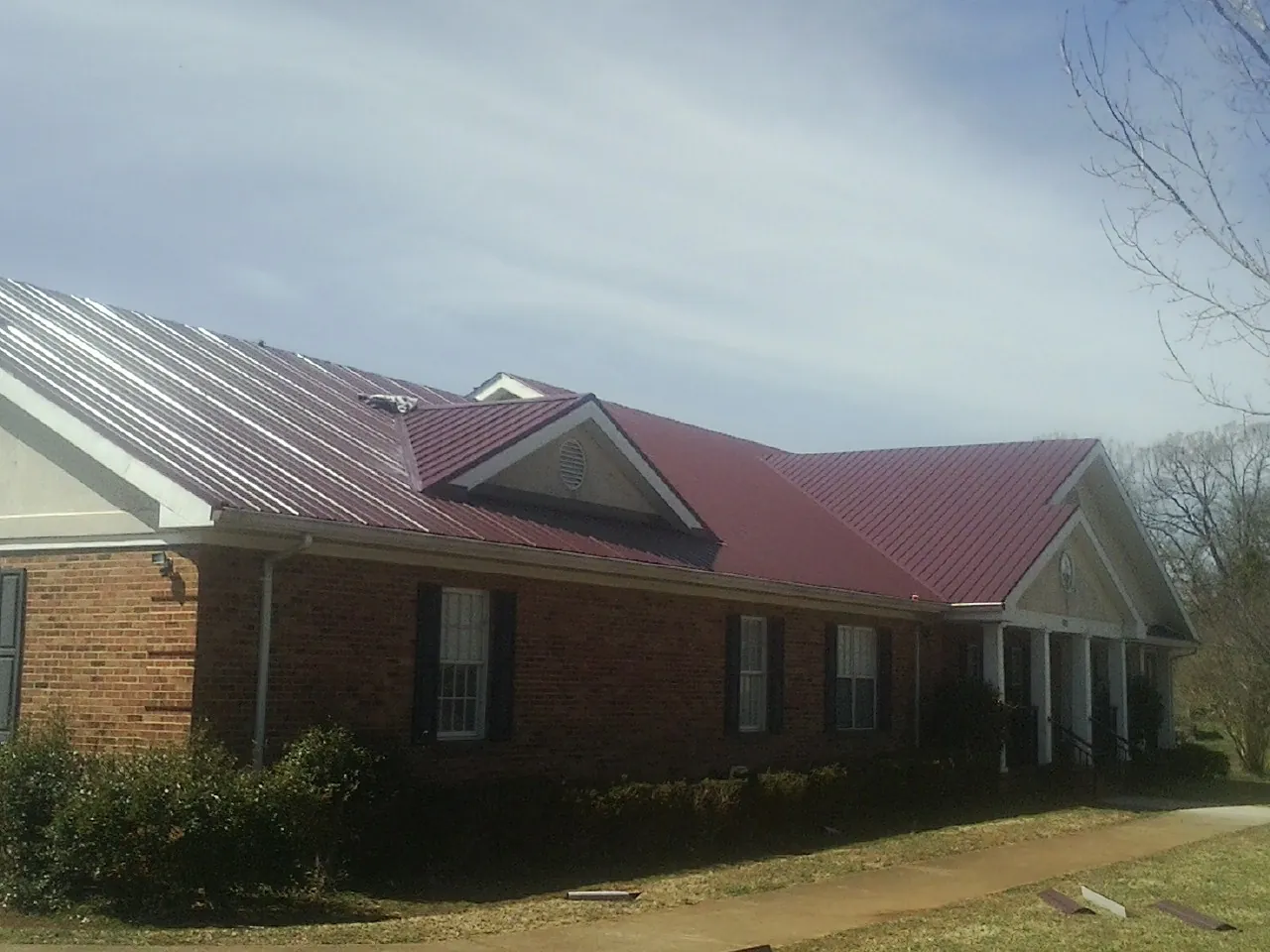 Red metal roof with gabled entries on a long brick building, from a Hail Damage Roof Repair job in Camas Valley