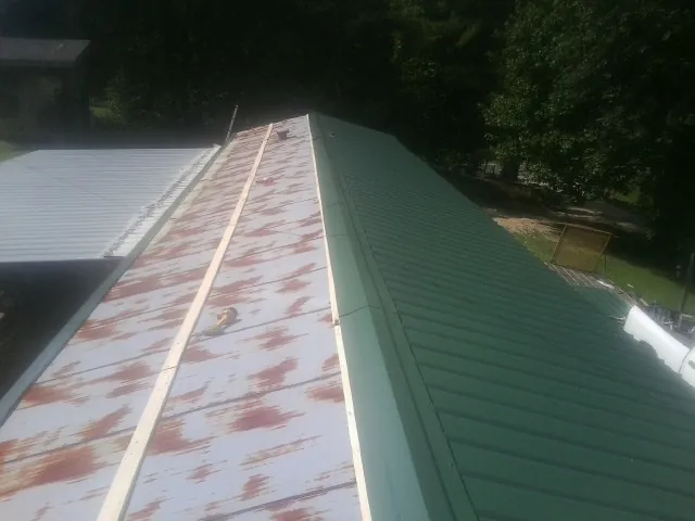 Old rusted panels beside newly installed green metal roofing — Wind Damage Roof Repair by Roofing Brothers in Camas Valley