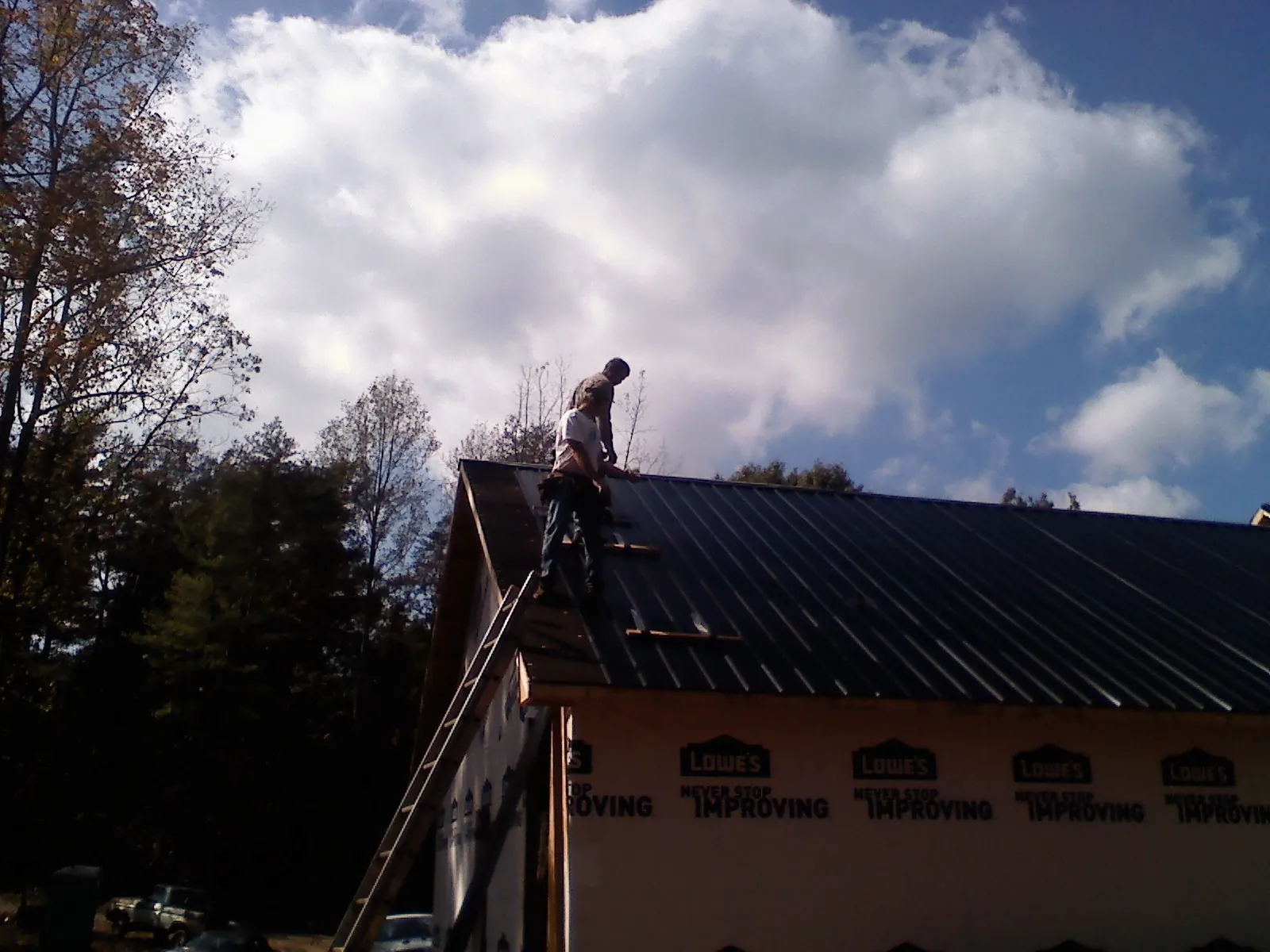 Roofer fastening dark metal panels high against a cloudy sky, from a Roof Inspection job in Camas Valley