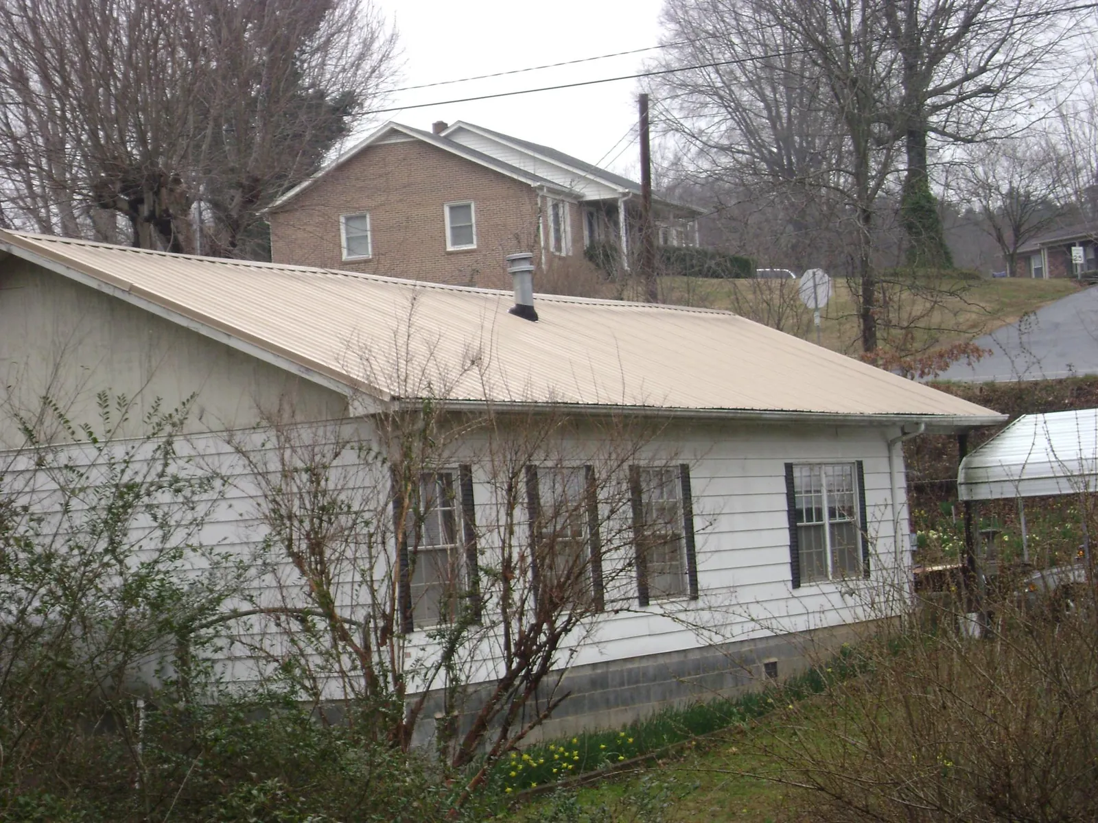 Tan metal roof on a white sided house set into a hillside — Commercial Roofing by Roofing Brothers in Camas Valley
